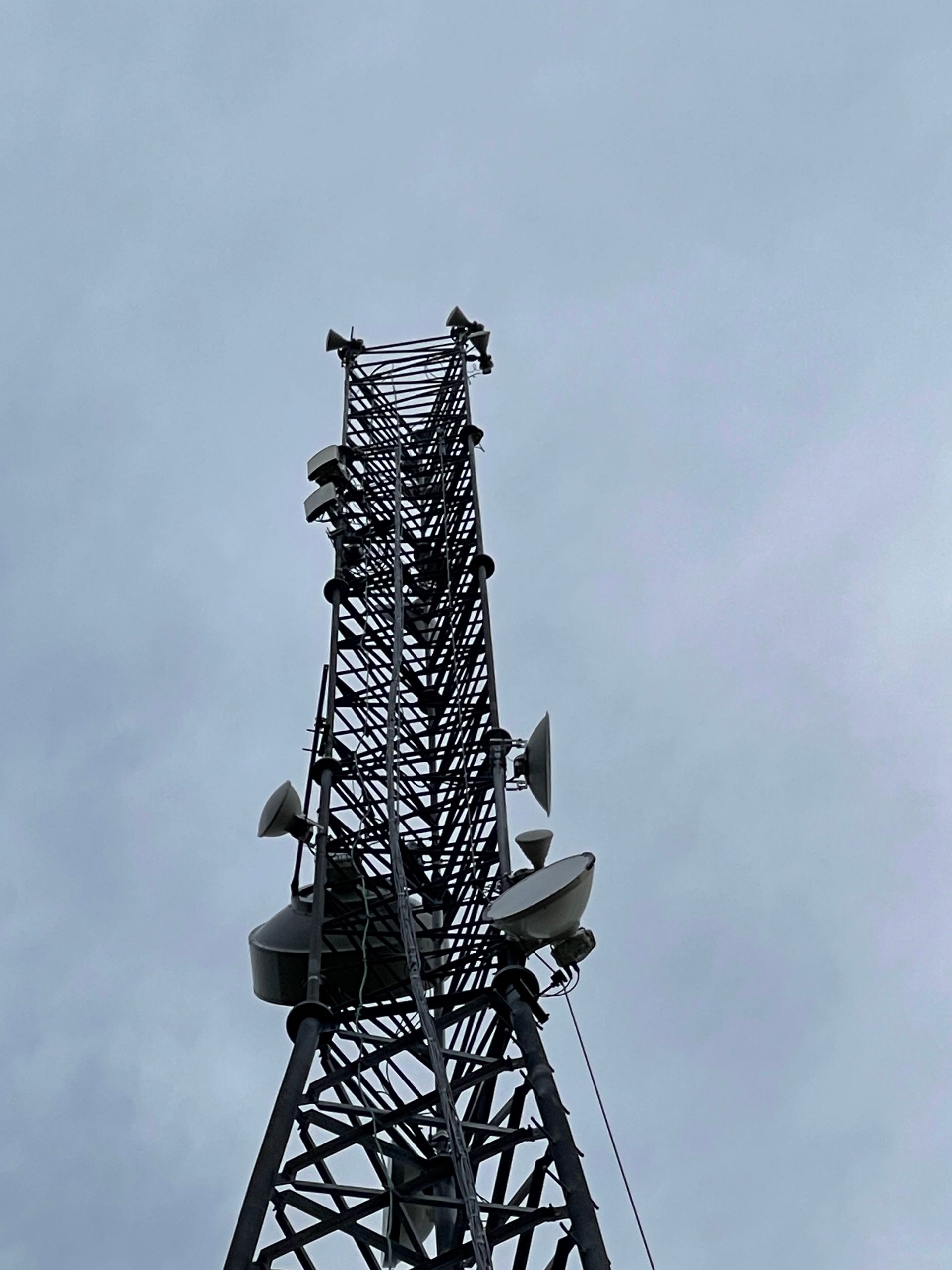 Telecommunication tower against a cloudy sky, with antennas and equipment attached.