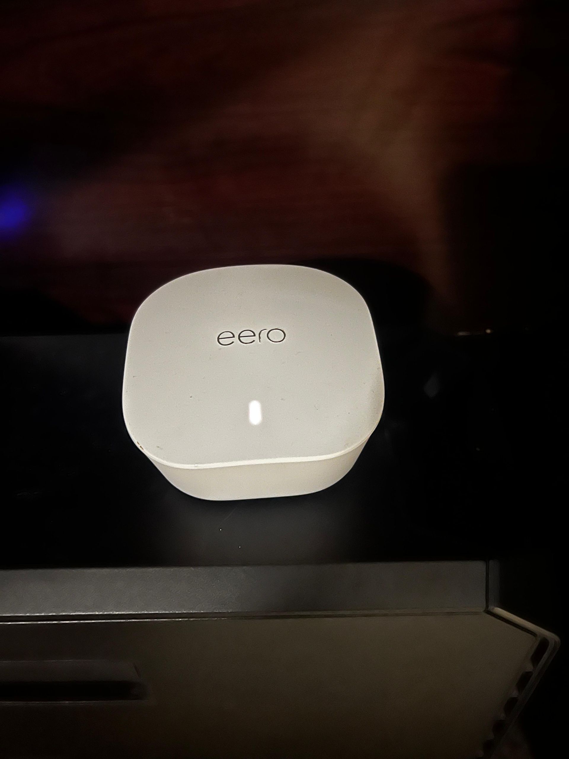White modem device on a black surface with a lit white indicator light.