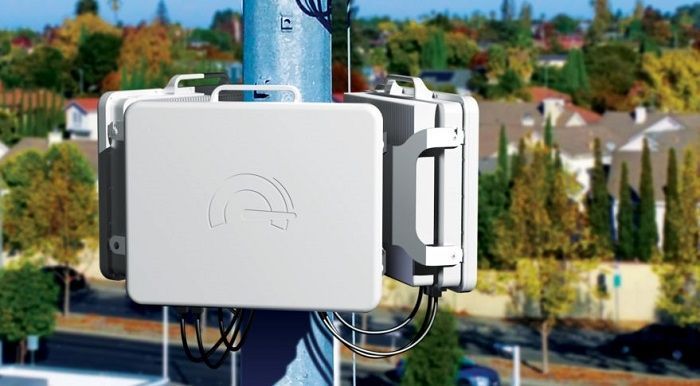 White wireless communication equipment attached to a blue utility pole, houses in background.