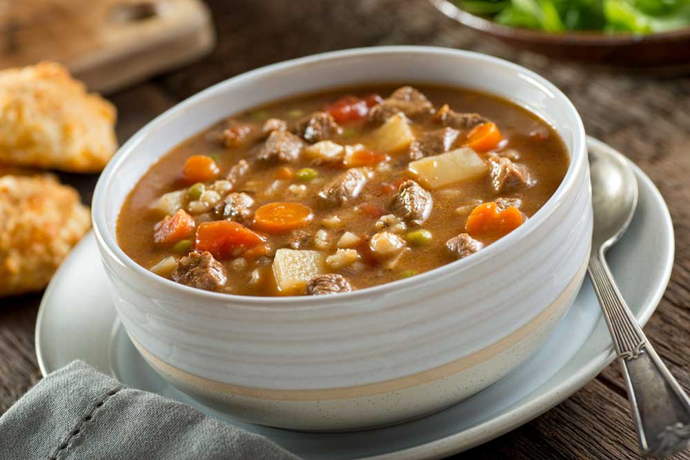 A bowl of delicious beef and barley soup with carrots, tomato, potato, celery, and peas