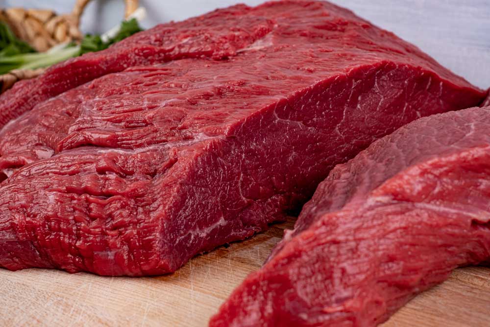 A piece of raw beef is sitting on a wooden cutting board.