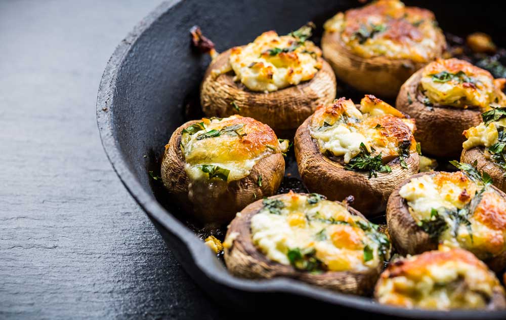Baked champignons mushrooms, filled with cheese, parsley and roasted garlic in black bowl