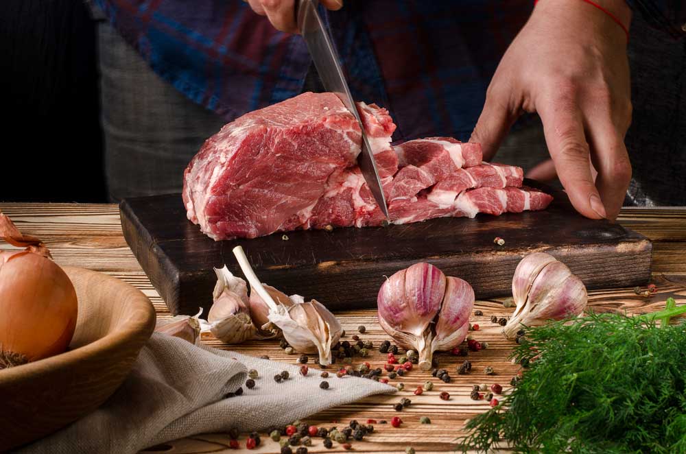Butcher cutting pork on wooden board on a wooden table
