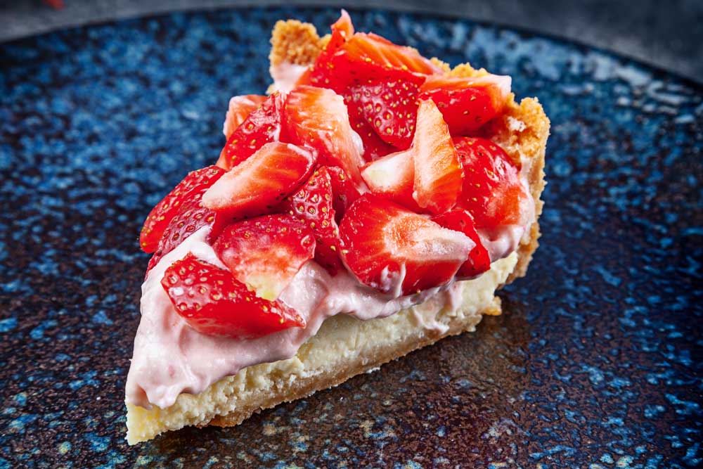 Close up view on fresh traditional strawberry cheesecake on dark plate