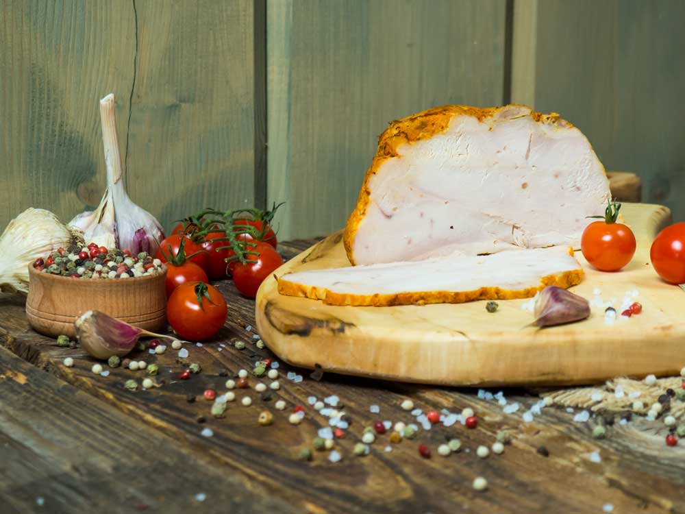 Cut piece of smoked pork on a wooden board with spices and tomatoes