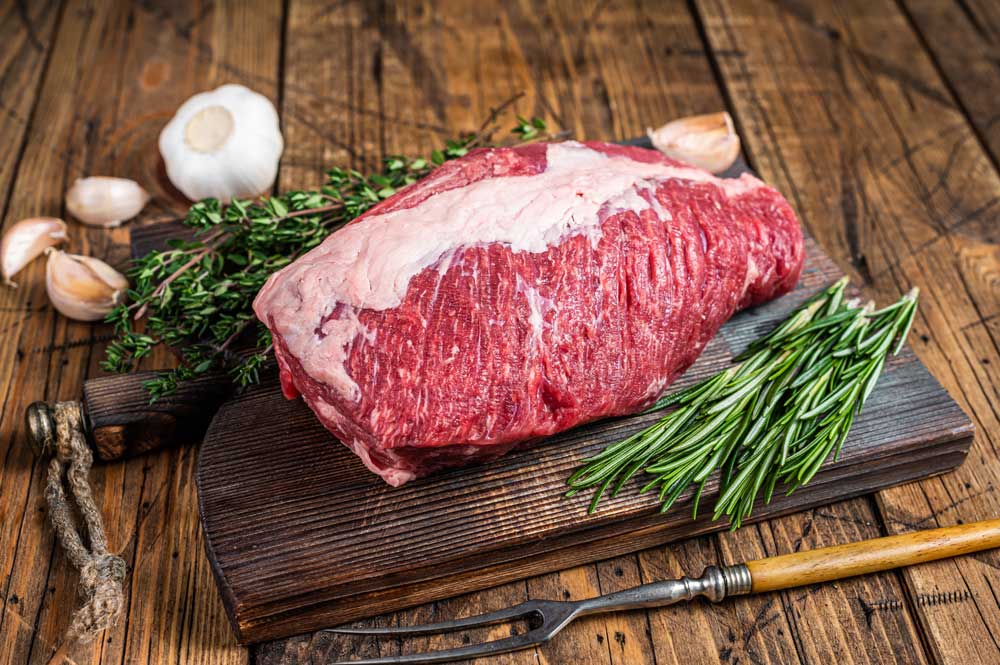 Fresh Raw brisket beef meat prime cut on a wooden board with herbs