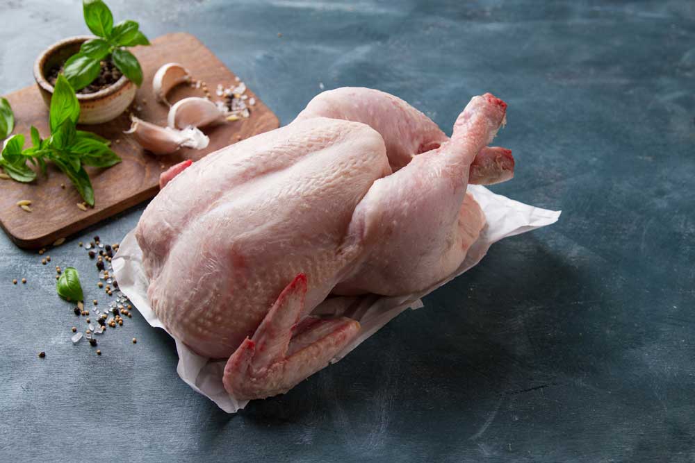 A raw chicken is sitting on a piece of paper on a table next to a cutting board.
