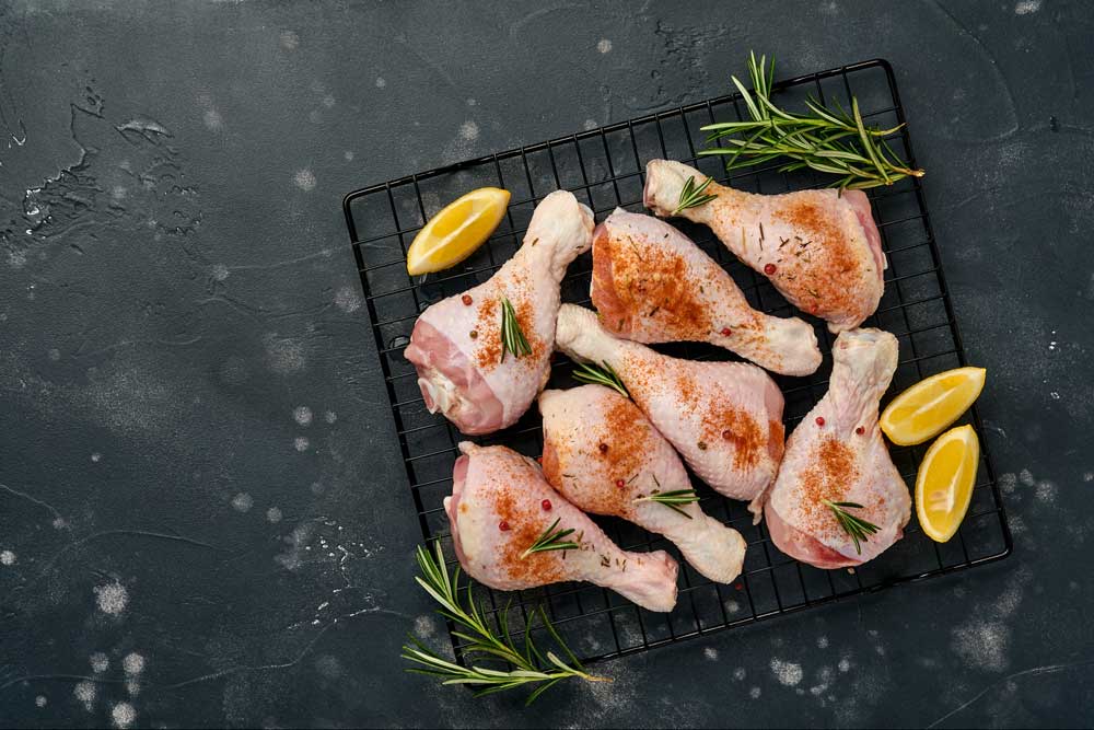 Raw chicken drumsticks with ingredients for cooking on a black stone background