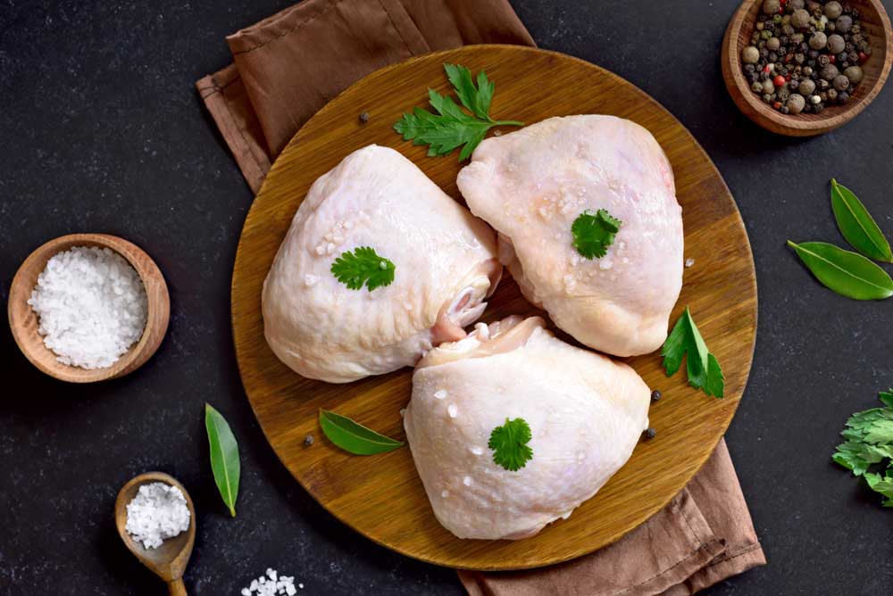Raw chicken thigh on wooden cutting board