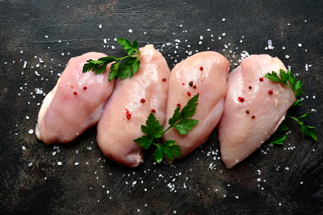 Raw chicken breasts with parsley and pepper on a black table.