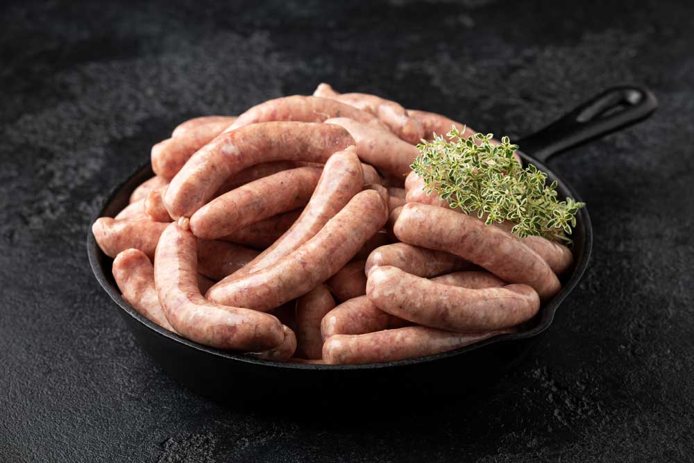 Raw pork chipolata sausage in cast iron skillet