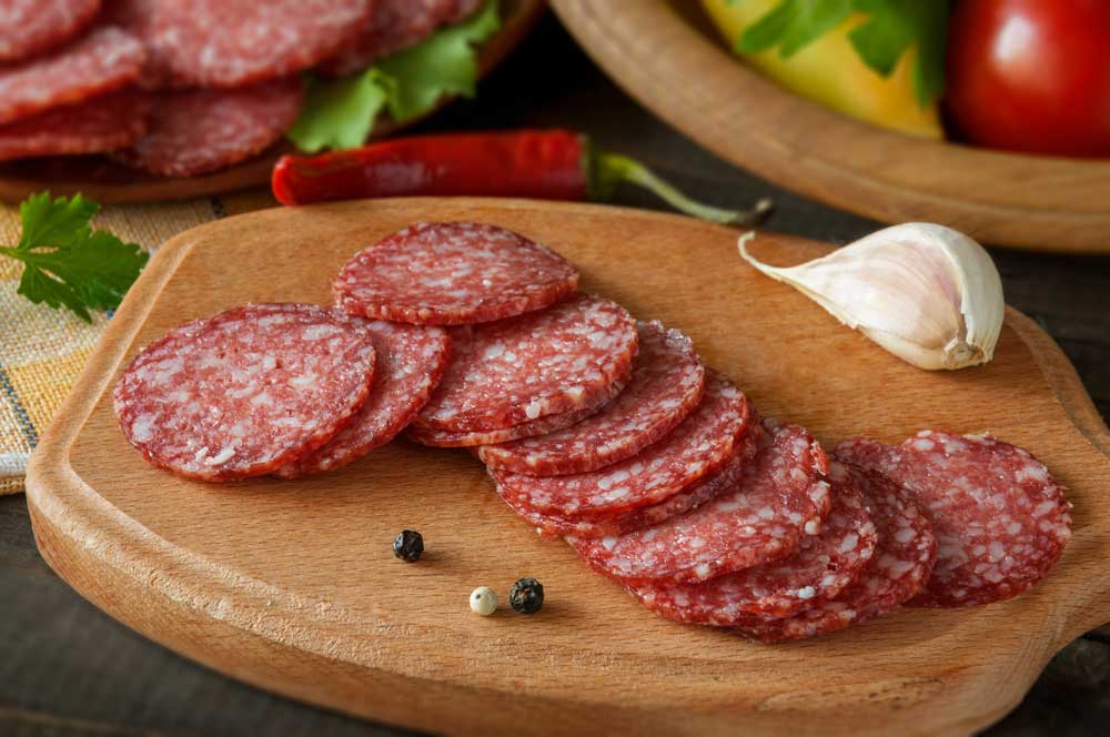 Slices-of-salami-with-vegetables-pepper-and-garlic-on-a-cutting-board