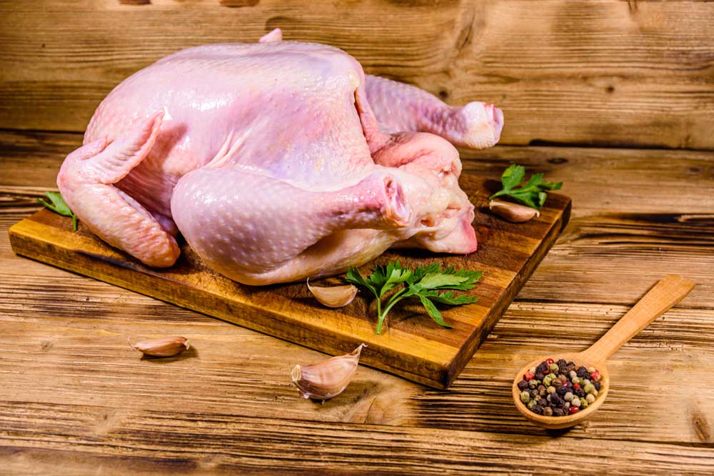 Wooden cutting board with the whole uncooked chicken, garlic and spices