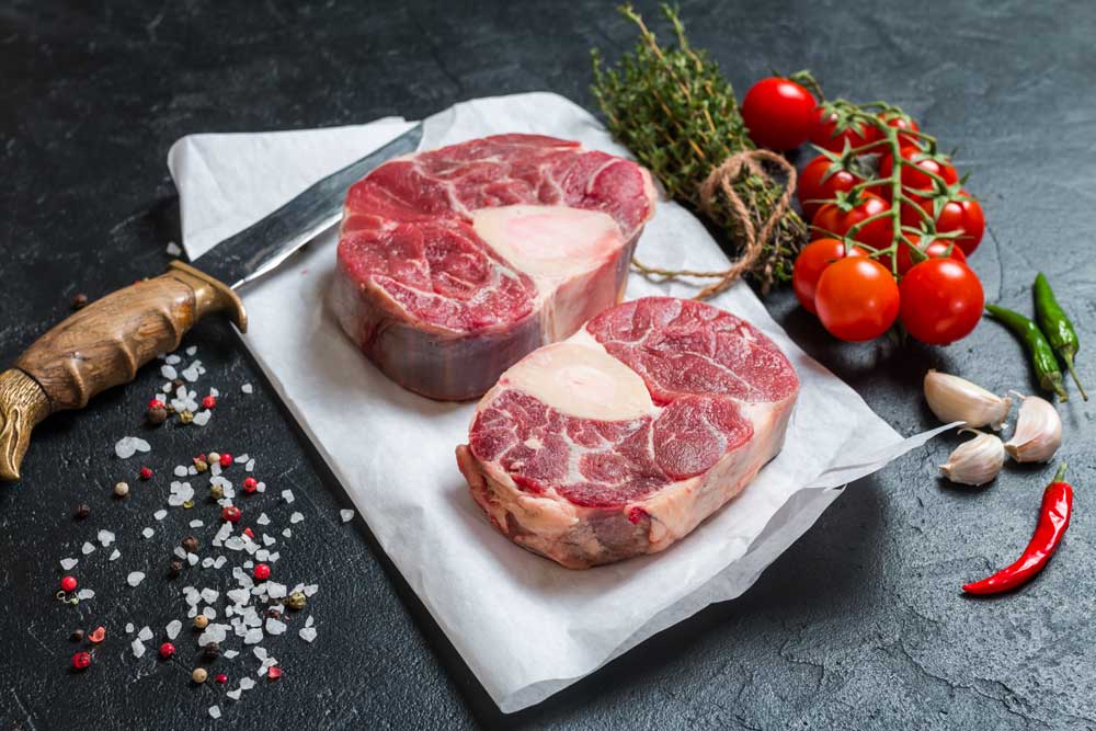 aw veal shank slices meat and ingredients for Osso Buco cooking on black background