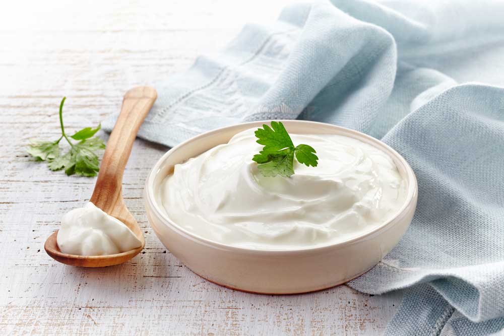 Sour cream in a small bowl with a dollop of sour cream on a wooden spoon