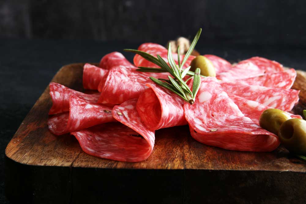 thinly sliced salami on a wooden cutting board