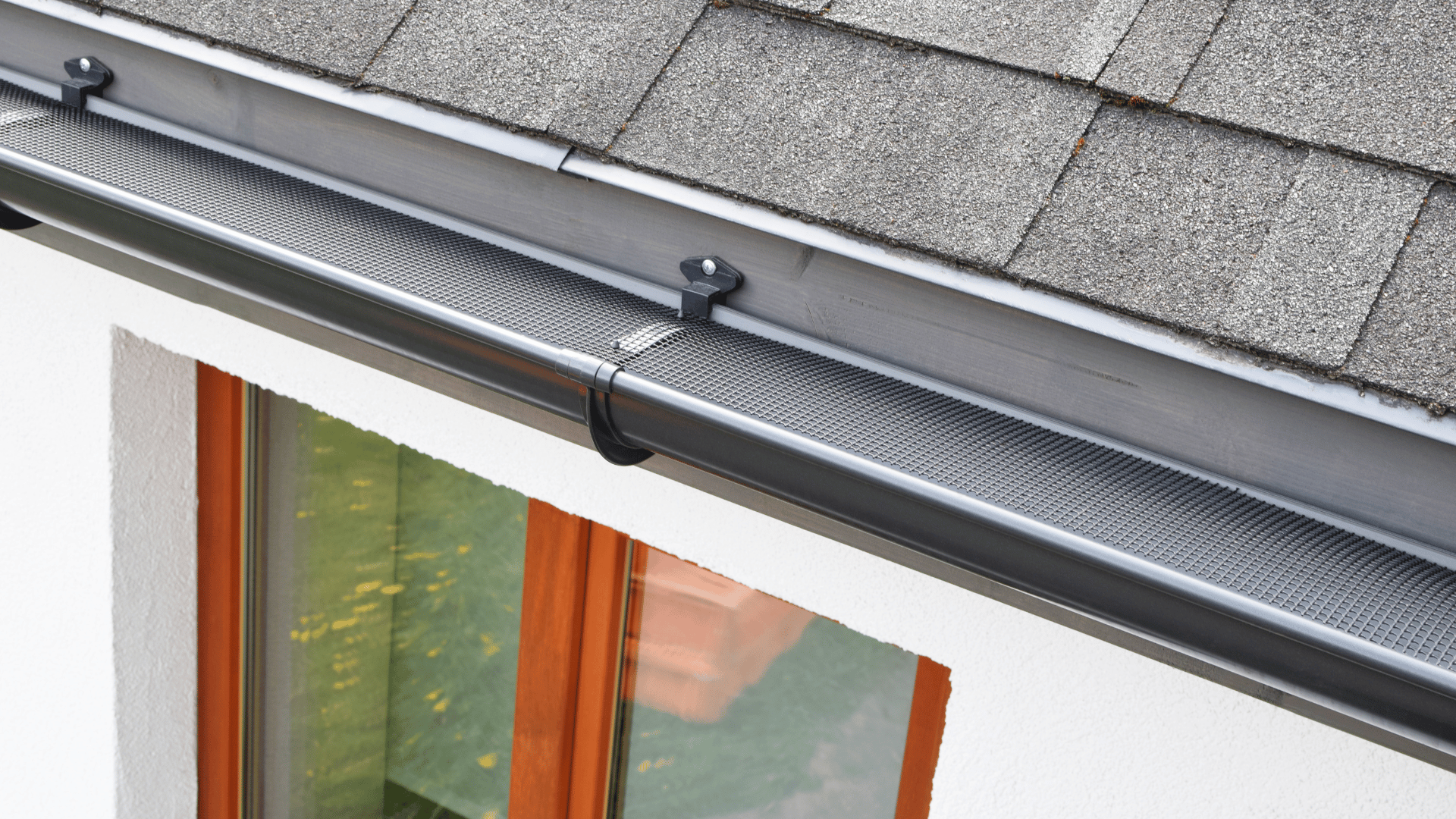 A close up of a gutter on a roof next to a window.