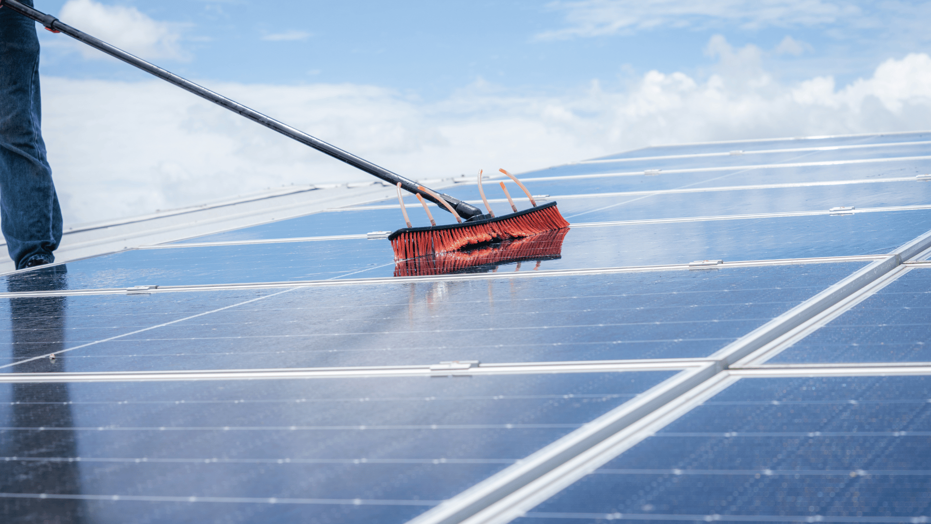 A man is cleaning solar panels with a broom.