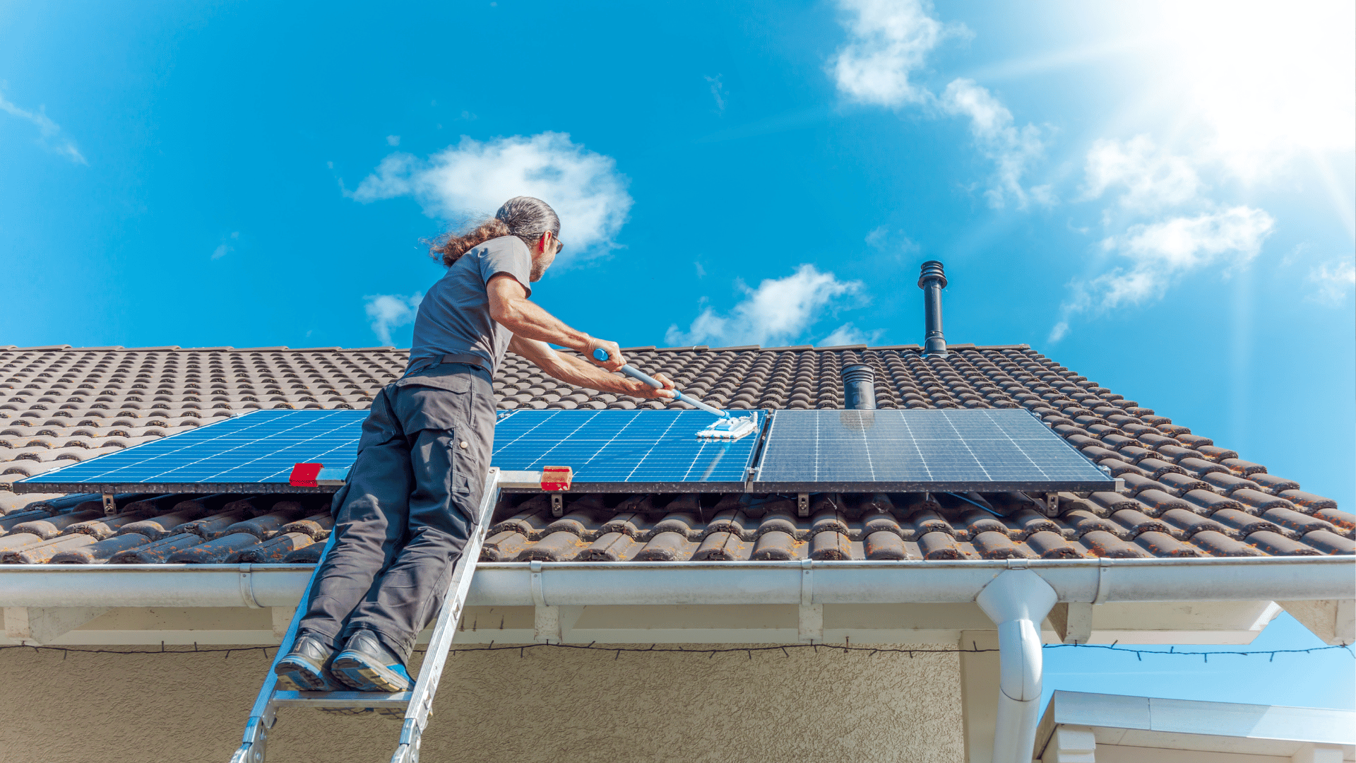 A man is installing solar panels on the roof of a house.