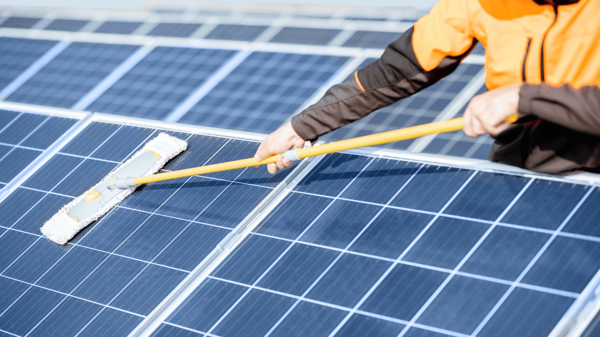 A man is cleaning solar panels with a mop.