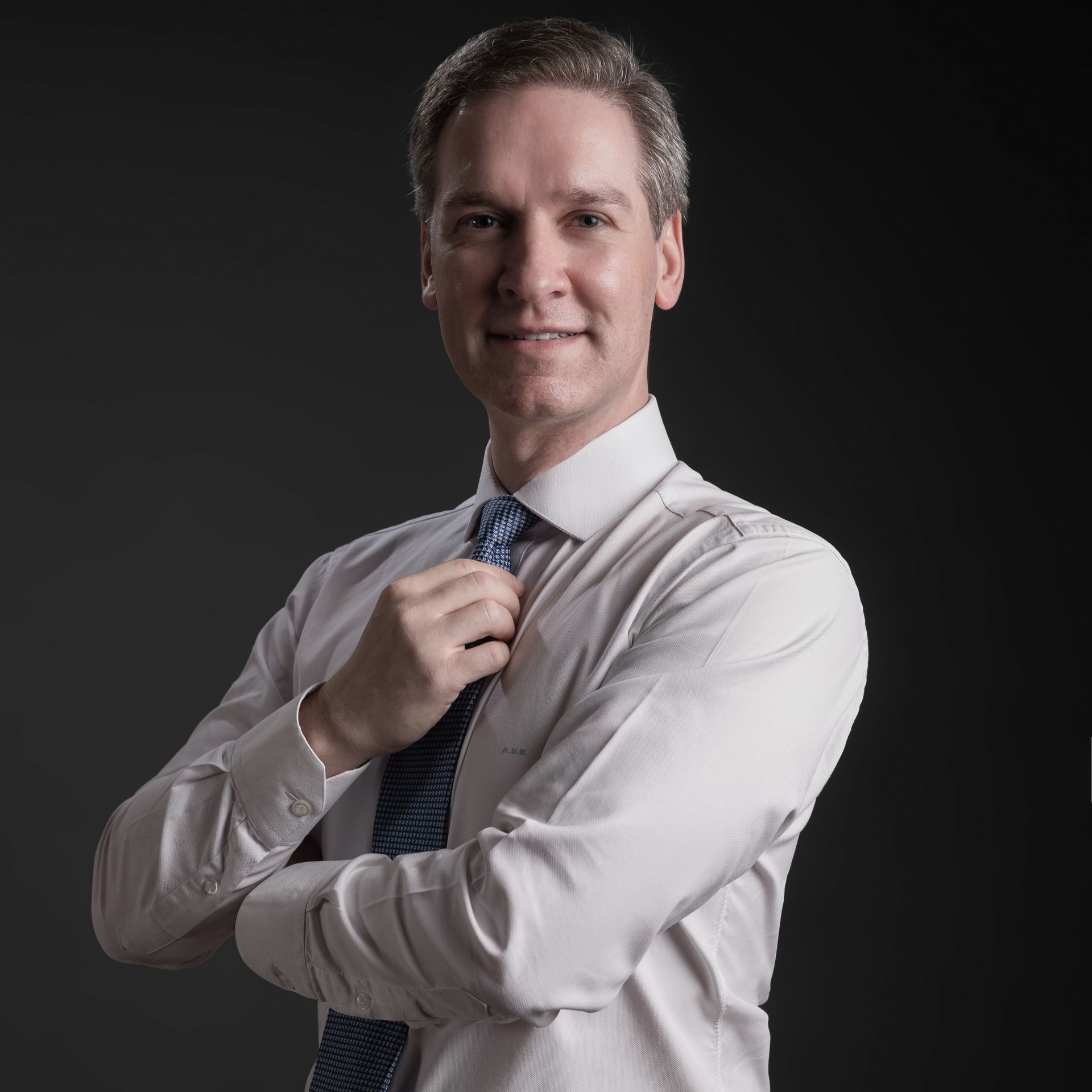 Foto artística Dr. Alexandre Bertoncini com camisa branca social em fundo escuro, olhando para a câmera com sorriso.