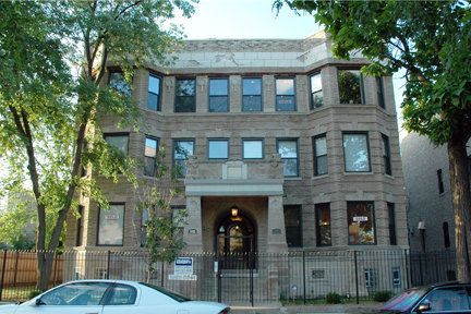 A white car is parked in front of a large brick building