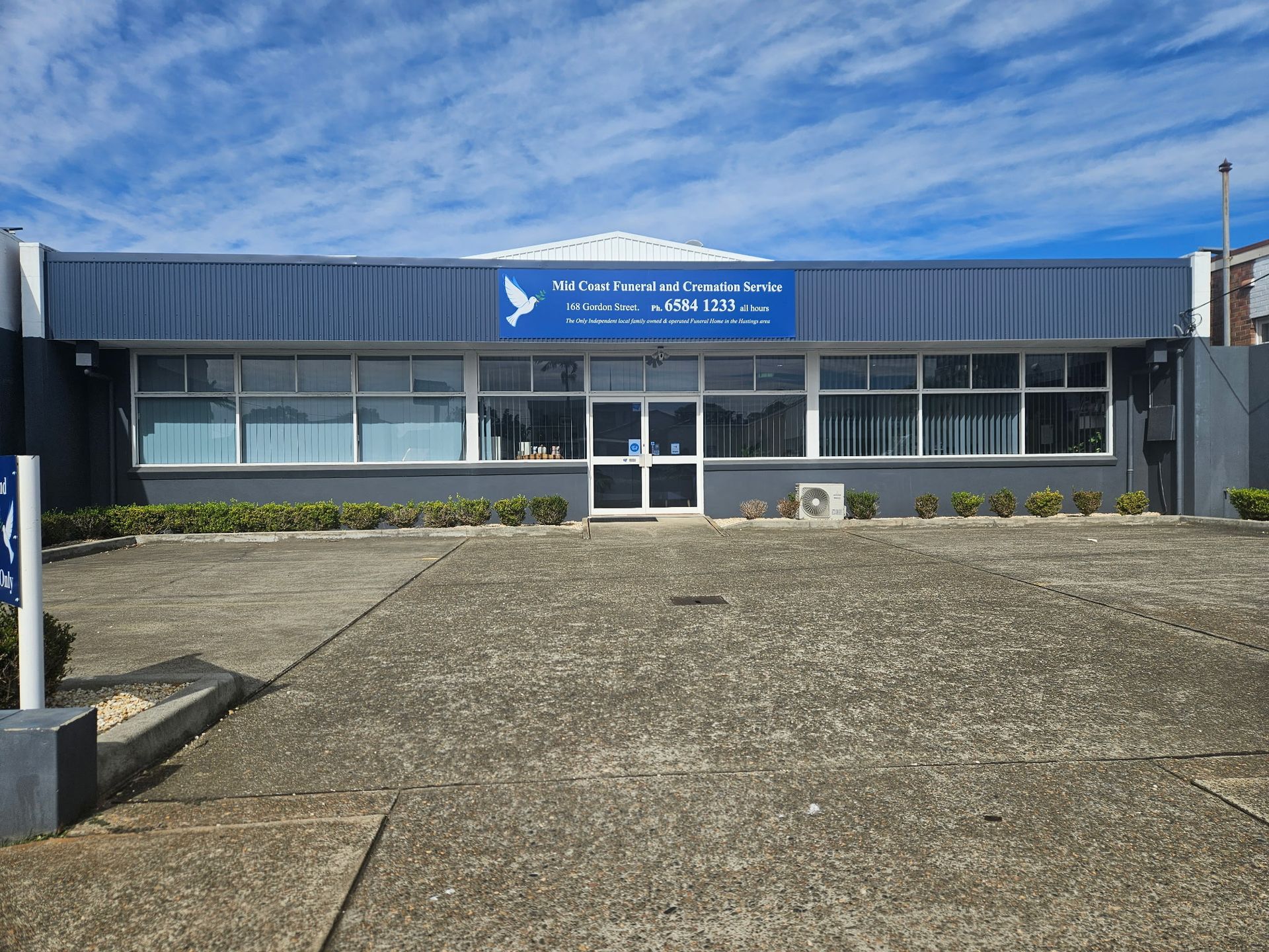 A Large White Building With a Blue Sign in Front of It — Mid Coast Funeral and Cremation Service In Port Macquarie, NSW