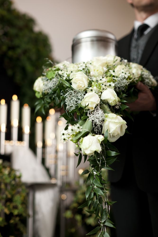 A Man is Holding a Bouquet of White Flowers — Mid Coast Funeral and Cremation Service In Taree, NSW
