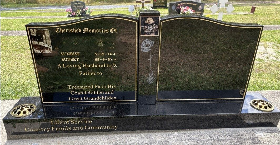 A dual-panel black granite headstone with engraved text and floral accents, situated in a grassy cemetery — Mid Coast Funeral and Cremation Service In Port Macquarie, NSW
