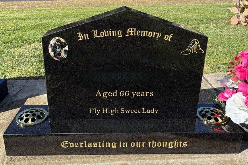A black granite headstone with gold text, a circular photo, and floral vases, set against a grassy background — Mid Coast Funeral and Cremation Service In Port Macquarie, NSW