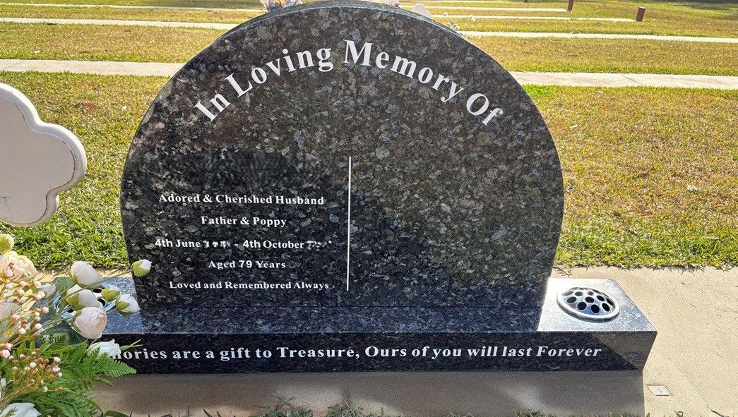 A semi-circular, dark granite gravestone in a cemetery, inscribed with