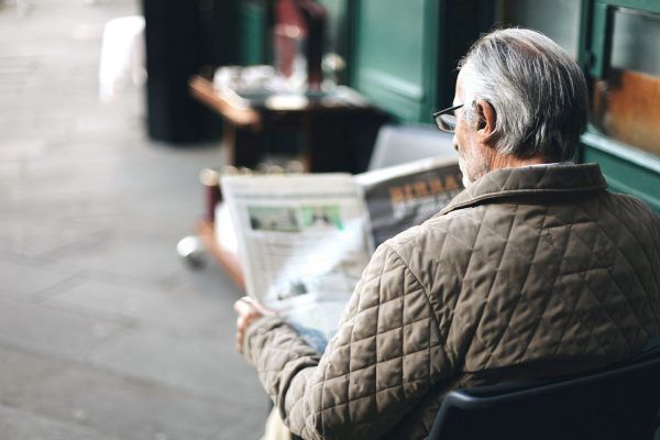 An Older Man is Sitting in a Chair Reading a Newspaper — Mid Coast Funeral and Cremation Service In Port Macquarie, NSW