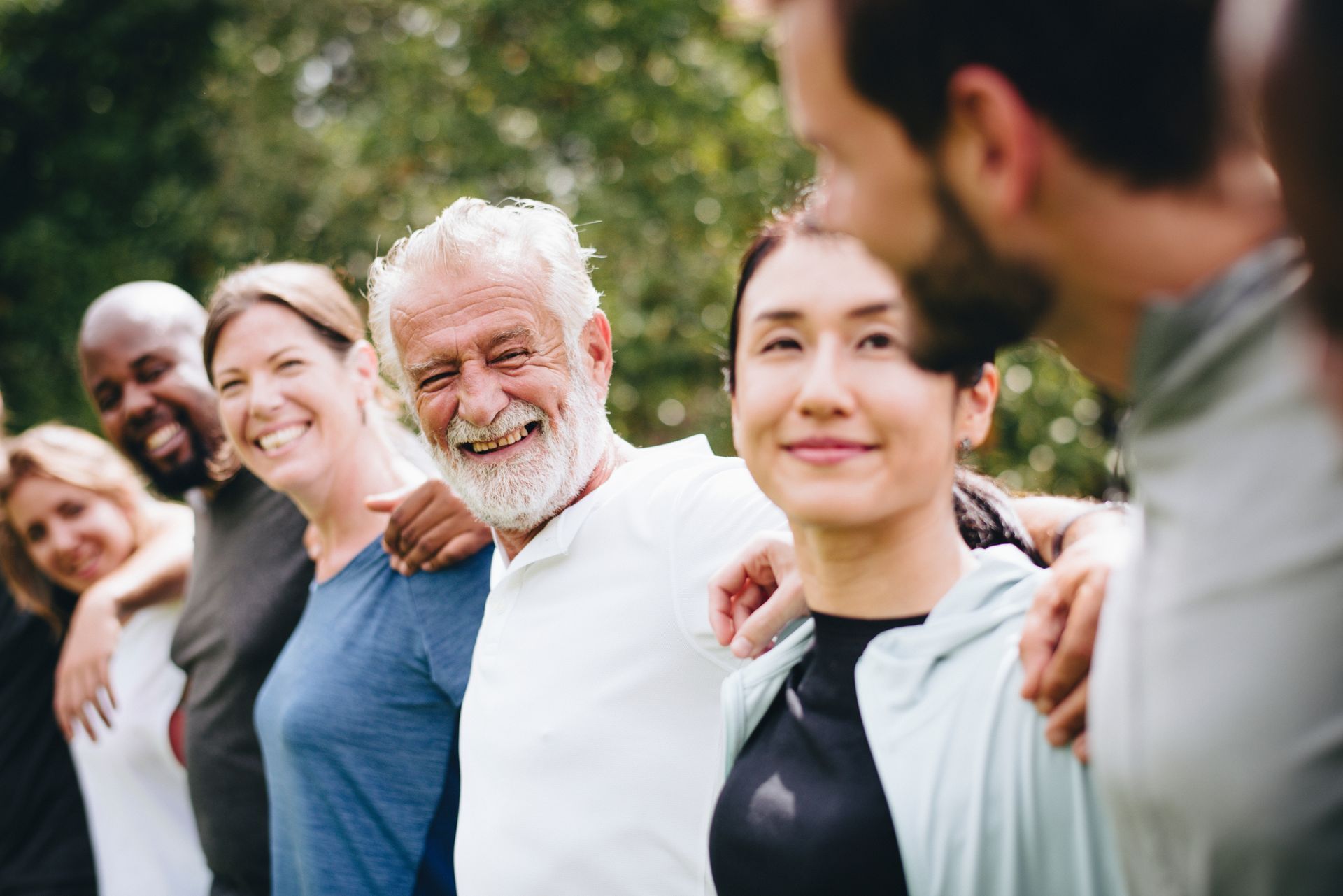 Group of diverse people with arms around each other, smiling outdoors.