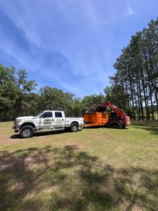 Red tractor with a front loader, dumping material into a yellow wood chipper, outdoors.