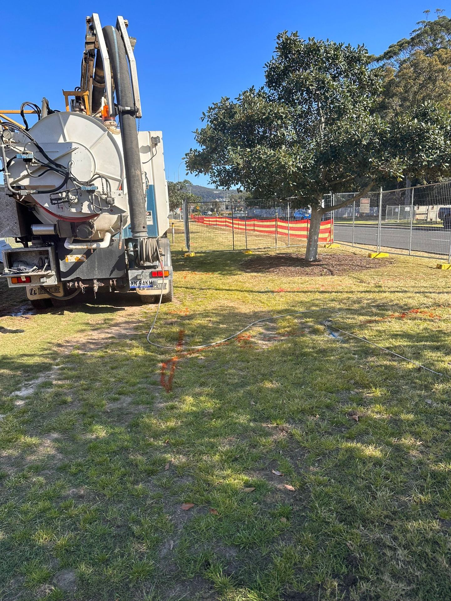 Trench with large black and red utility pipes installed on a construction site, with excavator in background