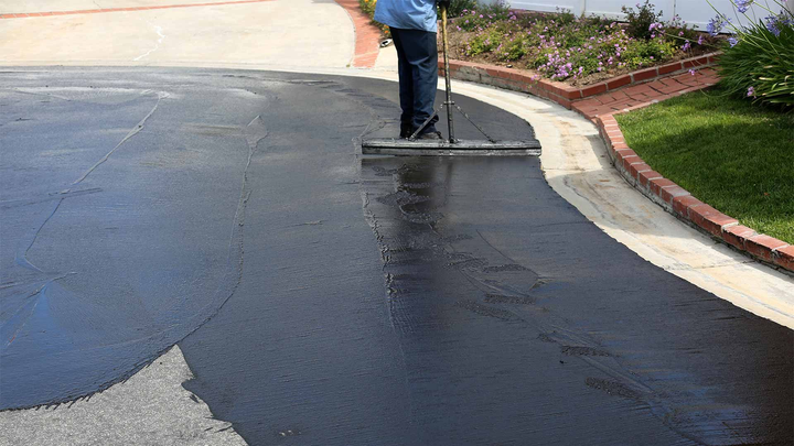 A man is spreading asphalt on a driveway with a broom.