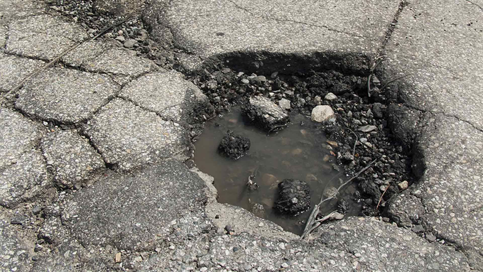 A large pothole in the middle of a road with water coming out of it.
