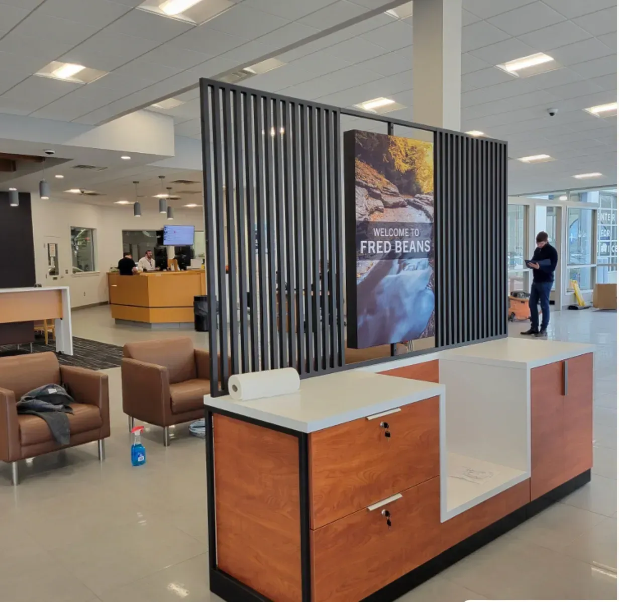 Modern lobby with seating and a wood-framed kiosk featuring a vertical digital ad screen