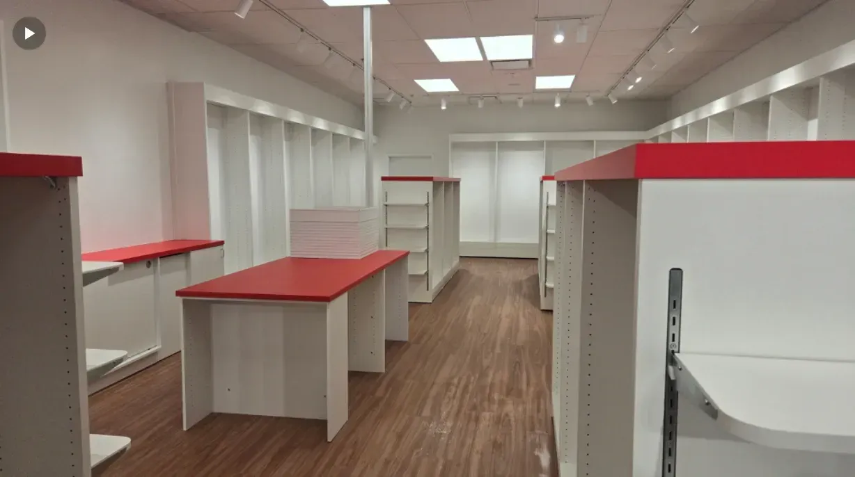 Empty retail store interior with white shelving and red counters on a wood floor.
