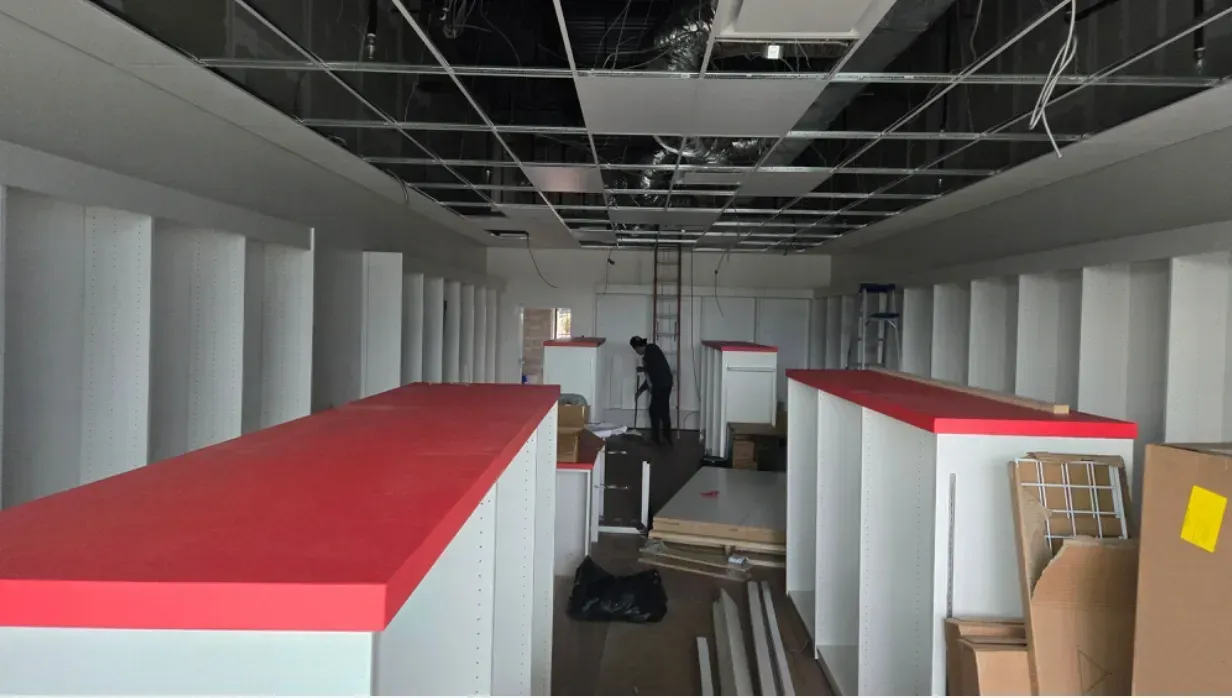 Empty store interior with red-topped shelves, unfinished ceiling, and boxes near the back wall