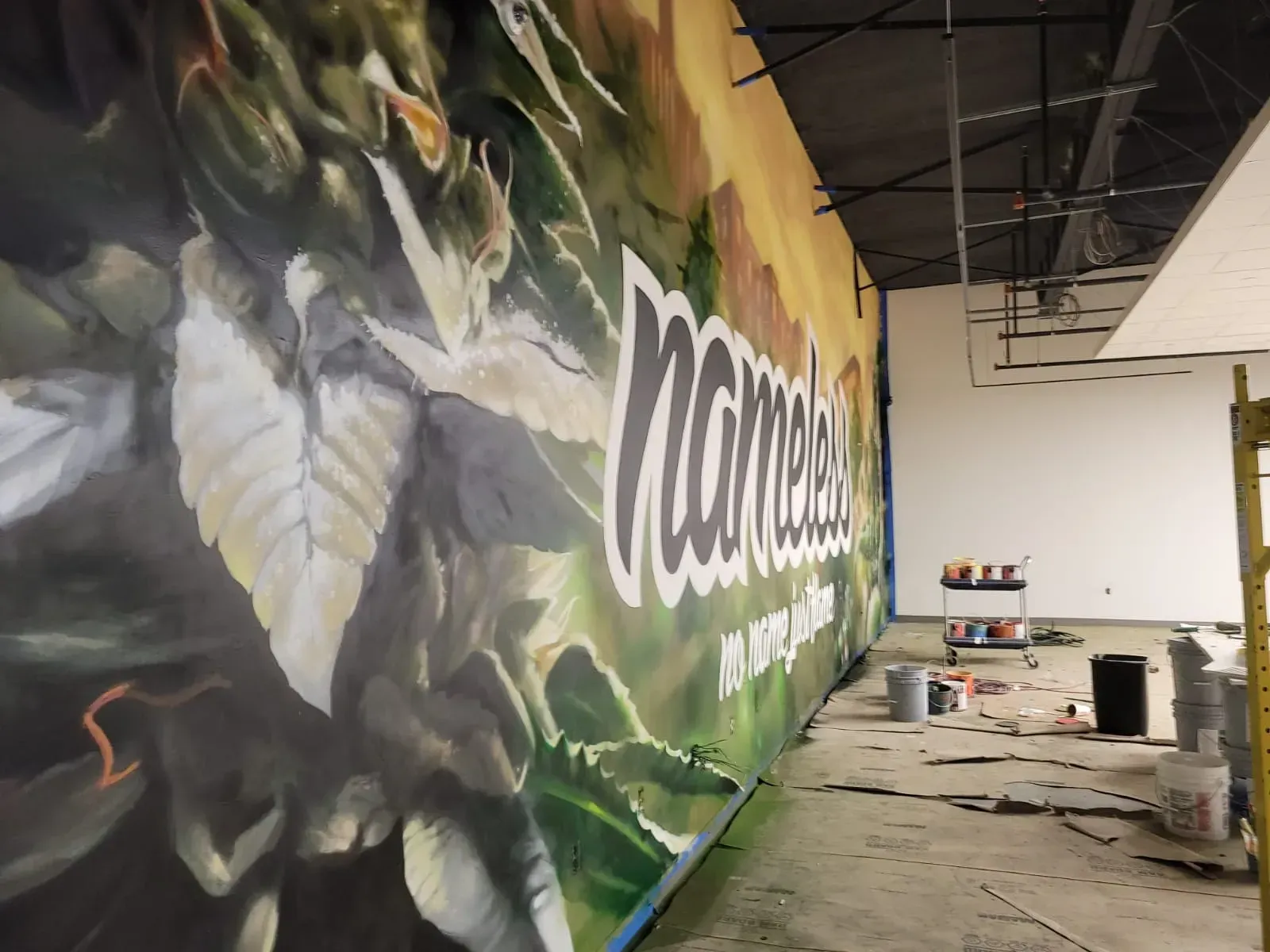 Large indoor mural with green leaves and white lettering on a wall in a partially finished room