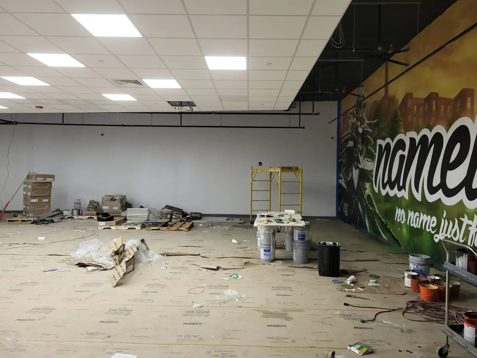 Empty room under renovation with debris on the floor, ladders, and a mural on the right wall.