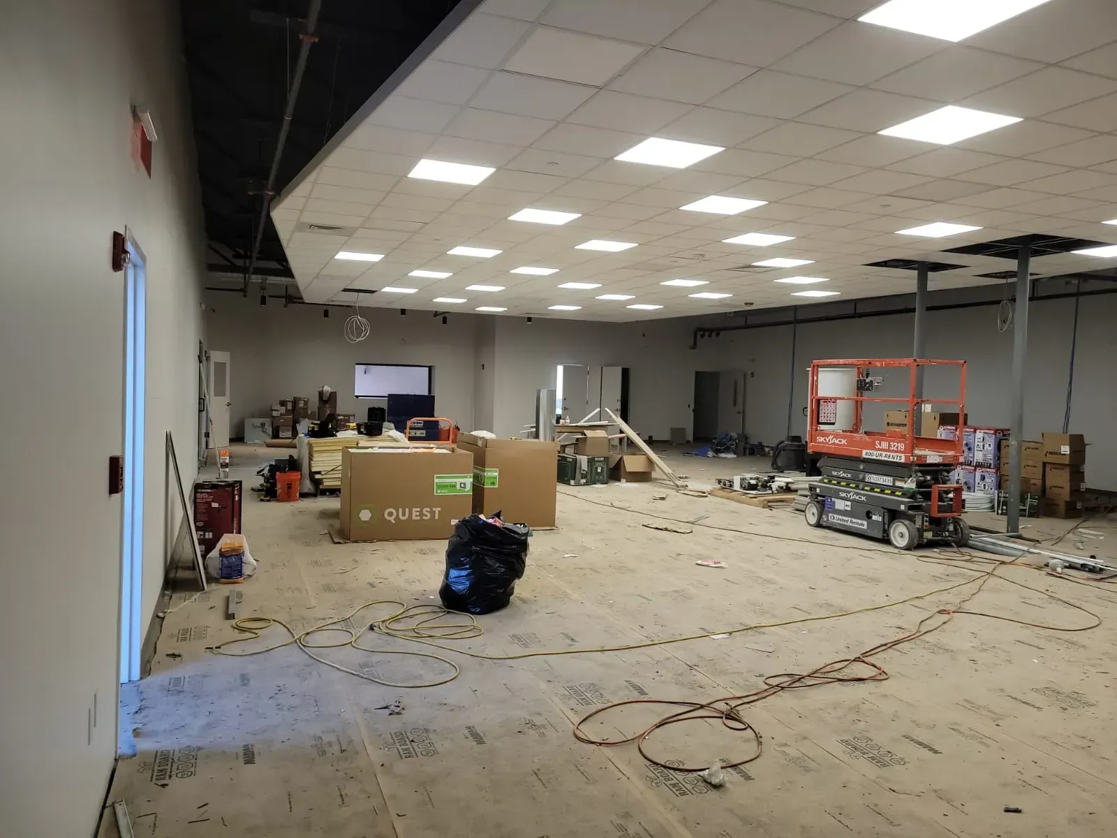 Empty warehouse interior with boxes, carts, and scattered cables under bright ceiling lights