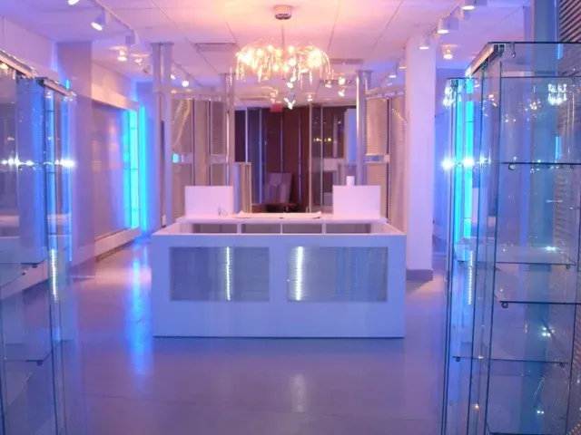 Modern lobby with white reception desk, blue lighting, chandeliers, and glass display cases on both sides