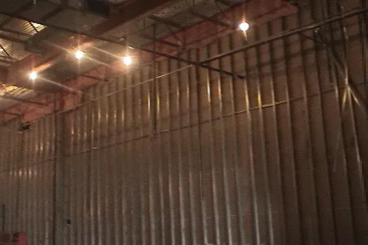 Dimly lit industrial interior with tall corrugated metal walls and overhead lights