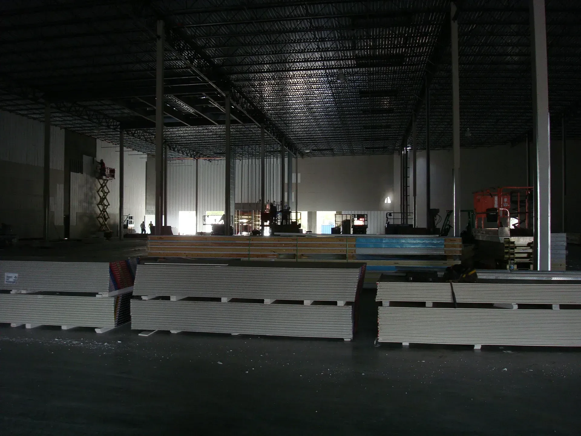 Dark construction site interior with metal framing, lights, and stacked materials in the foreground