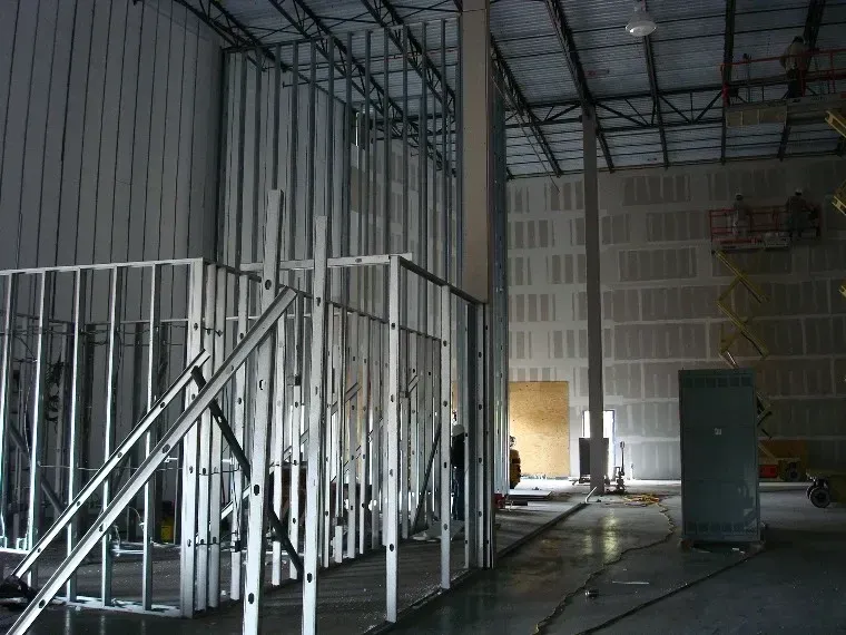 Partially framed interior room with metal studs, drywall, ladder, and construction materials on the floor