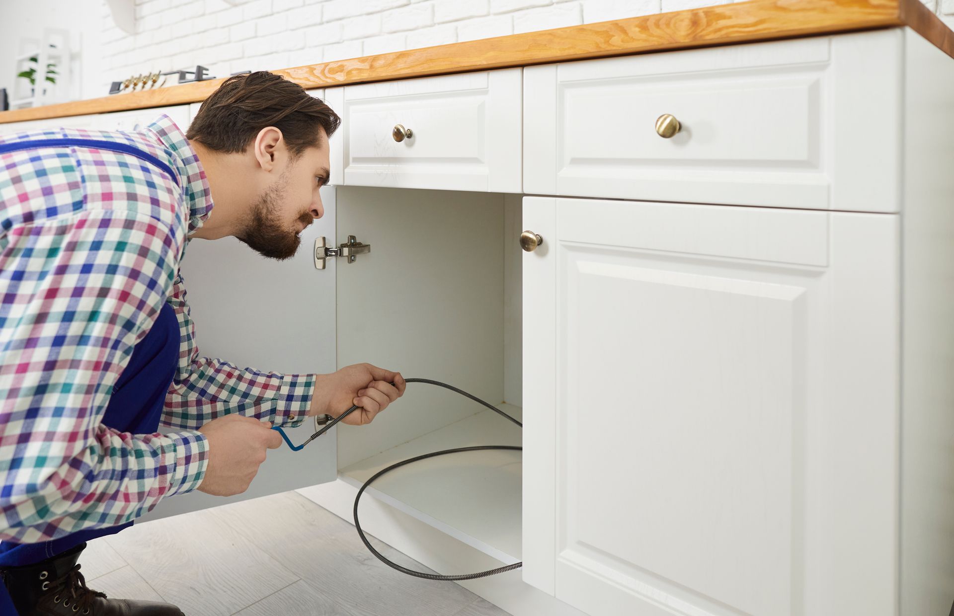 A plumber unclogging a kitchen sink with a professional force-pump cleaner.