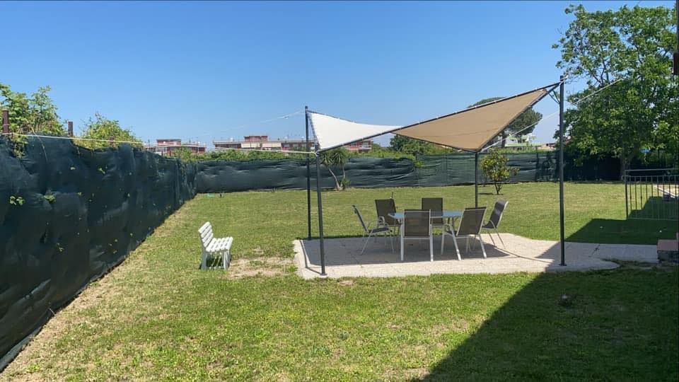 Un cortile con patio, tavolo, sedie, ombrellone ed erba. Una panchina bianca si trova sulla sinistra.