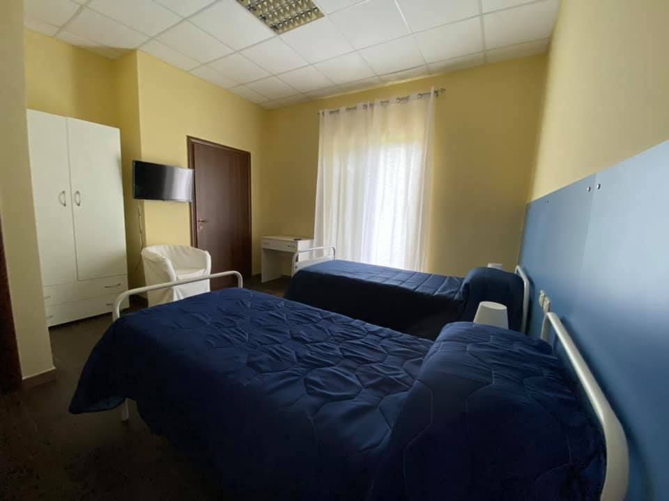 Due letti in una stanza con pareti gialle, armadio, TV, sedia e una finestra con tende.